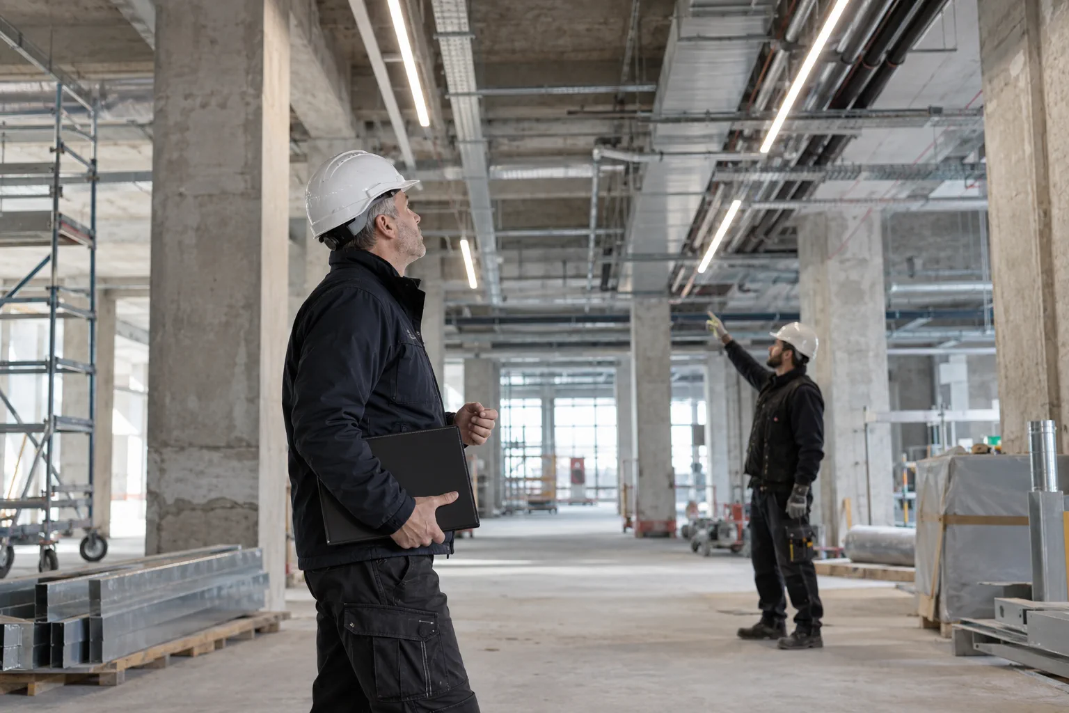 Bauleitung: Bauleiter mit Projektmappe stimmt sich auf der Baustelle mit einem Handwerker über die Deckeninstallation ab